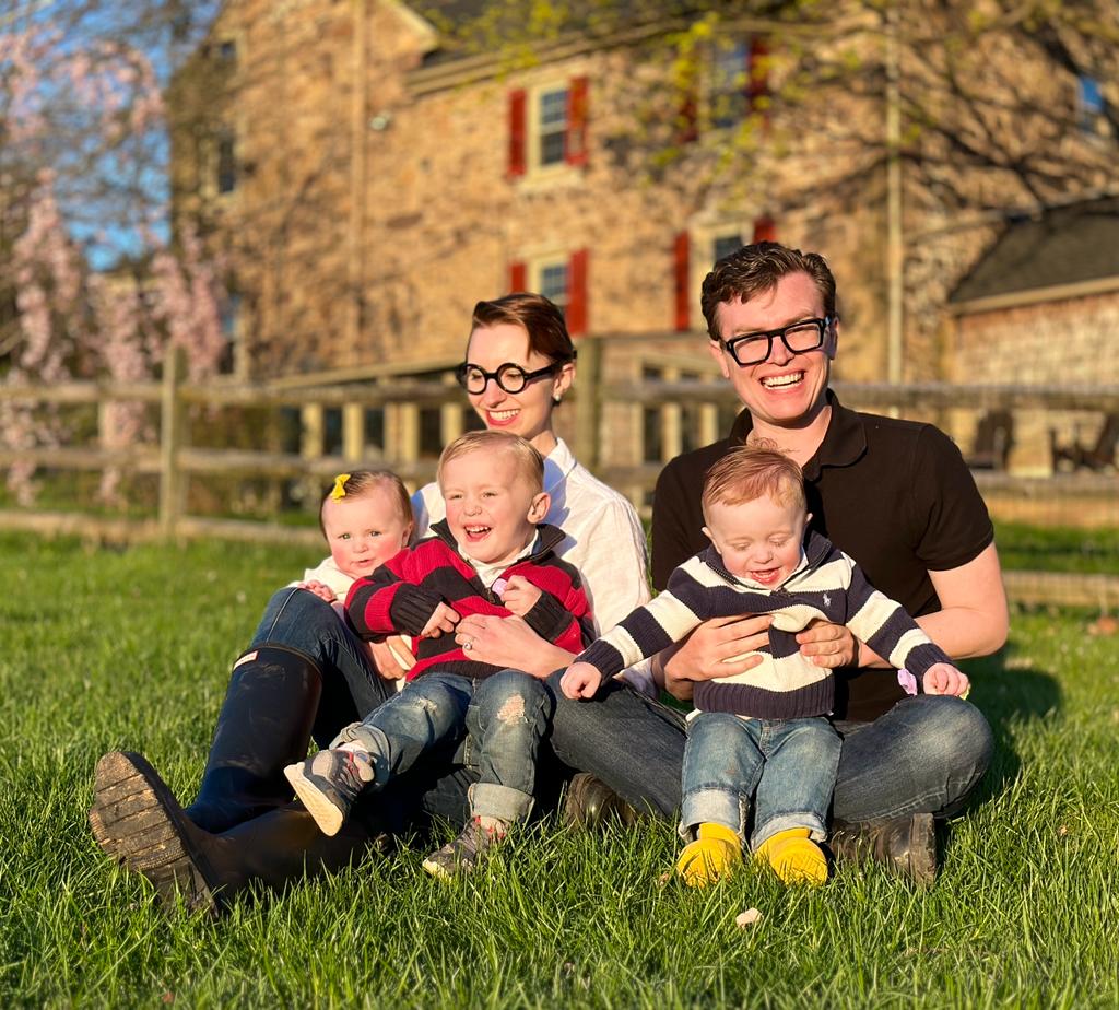 Ein weißes Paar sitzt vor einem Haus mit 3 kleinen Kindern