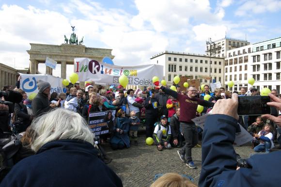 Menschen mit Trisomie 21 stehen mit Schildern vor dem Brandenburger Tor